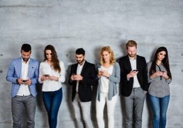 Group of business people standing against the wall and typing message on their smart phone